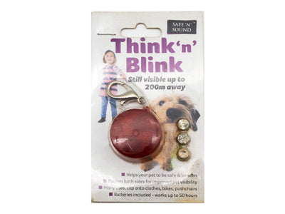 A red reflective dog safety keychain on its original retail backing card, branded 'Think 'n' Blink' by 'Safe 'N' Sound'. The packaging features a child and a dog illustration, showing the keychain attached with a metal clip.