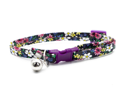 A pet collar with a colorful floral pattern on a black background, featuring a purple plastic buckle and a silver metal bell.