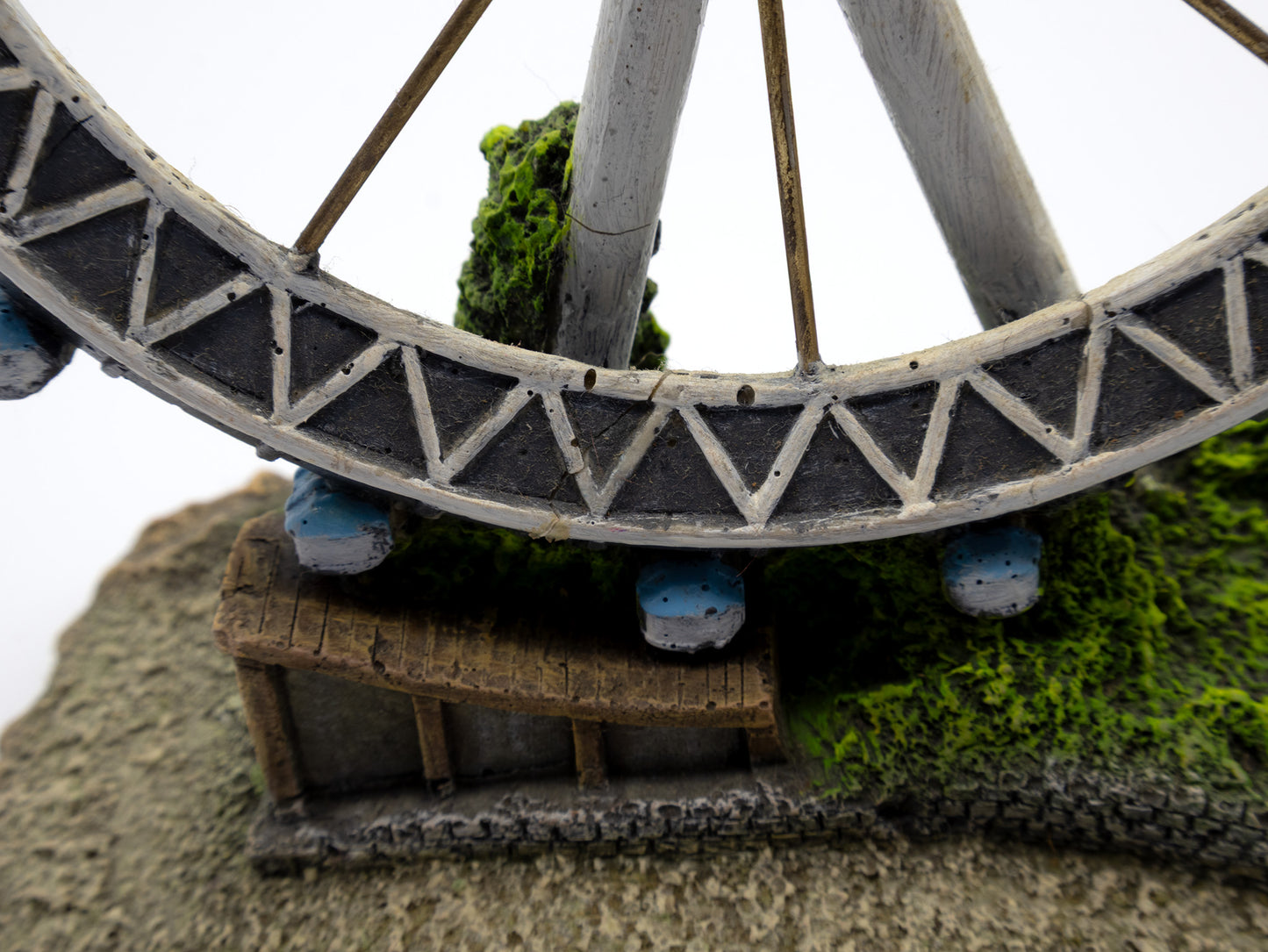 Model of a Ferris wheel with a small building underneath on a textured surface.