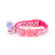 A pink pet collar with a matching pink plastic buckle, decorated with silver and white star sequins. It features a small dangling charm with a pink flamingo and a blue flower.