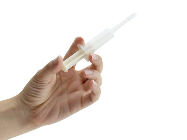 A hand holding a translucent white plastic syringe-like applicator or tool against a plain white background.