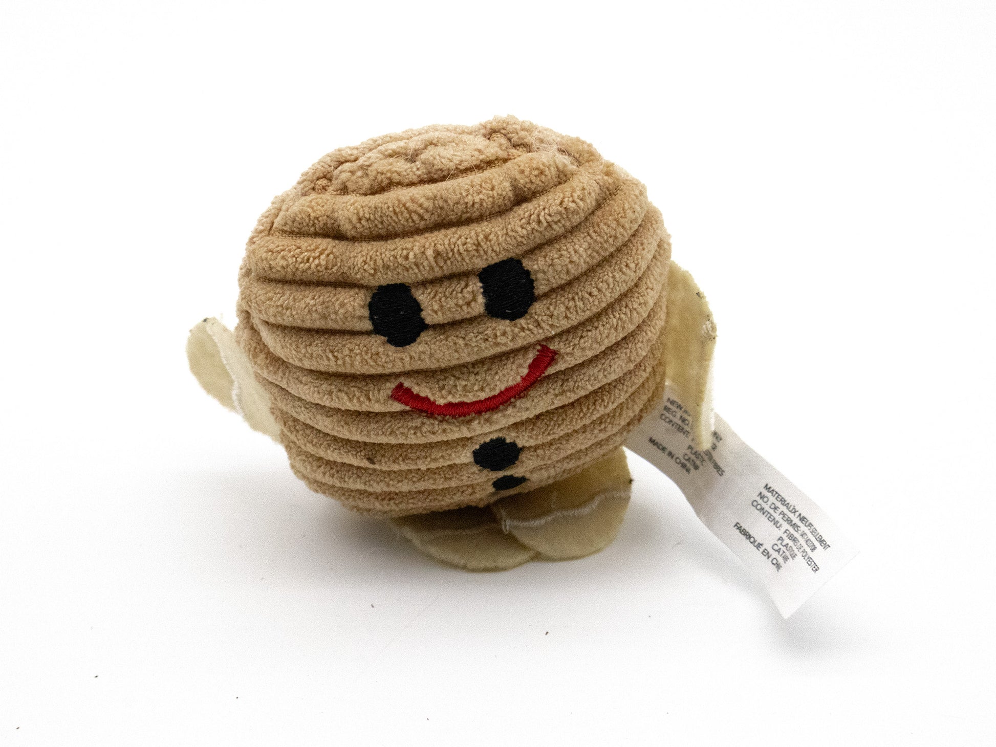 A small plush toy shaped like a round, ribbed beige character with black embroidered eyes and mouth, a red smile, and a white hangtag attached, photographed on a white background.