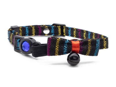 A pet collar with a black woven strap featuring multicolor stripes of yellow, blue, pink, and purple. It has a black plastic buckle with a blue gem, a matching striped fabric bow with a red ribbon accent, and a small black bell.