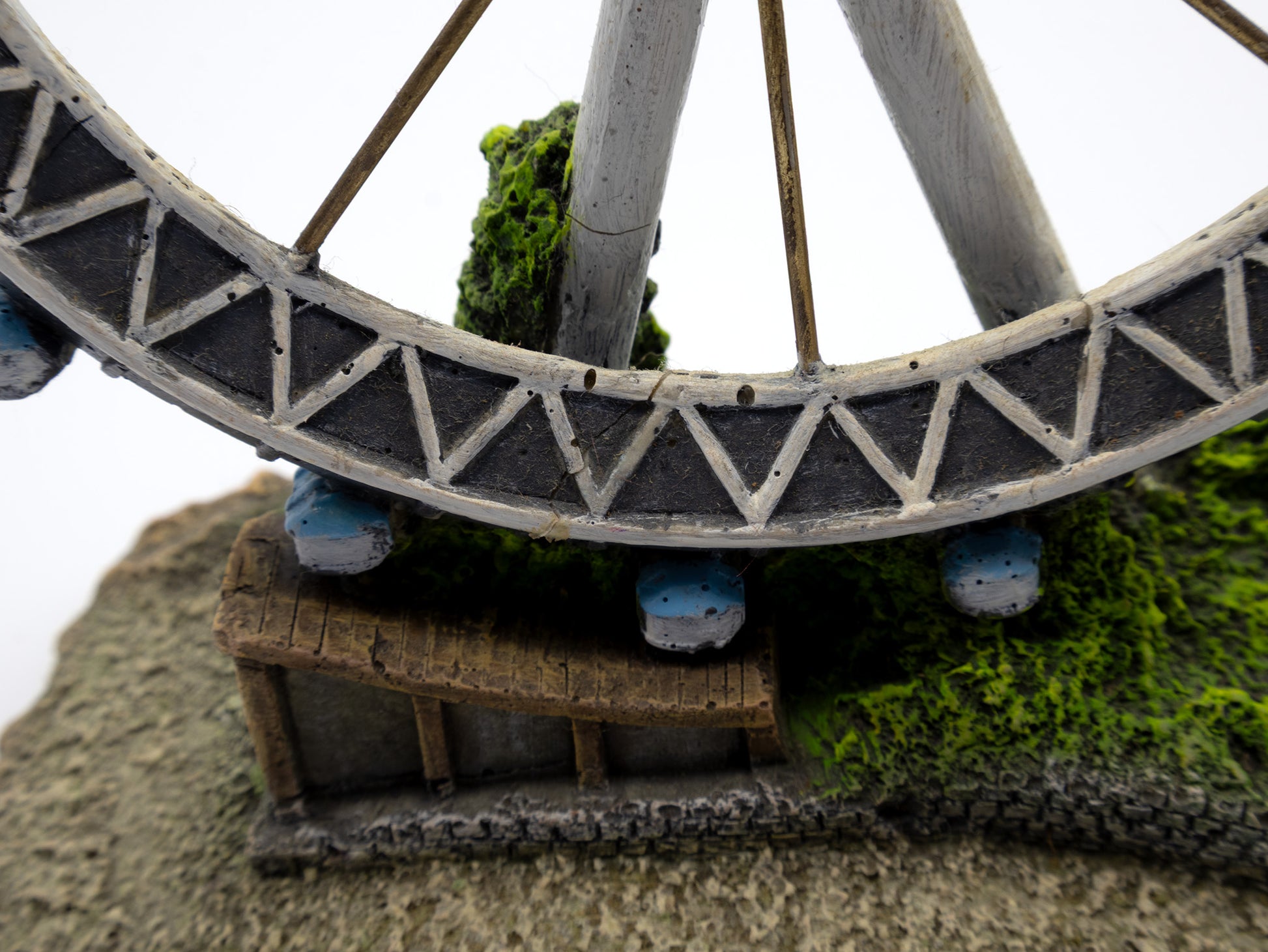 Model of a Ferris wheel with a small building underneath on a textured surface.