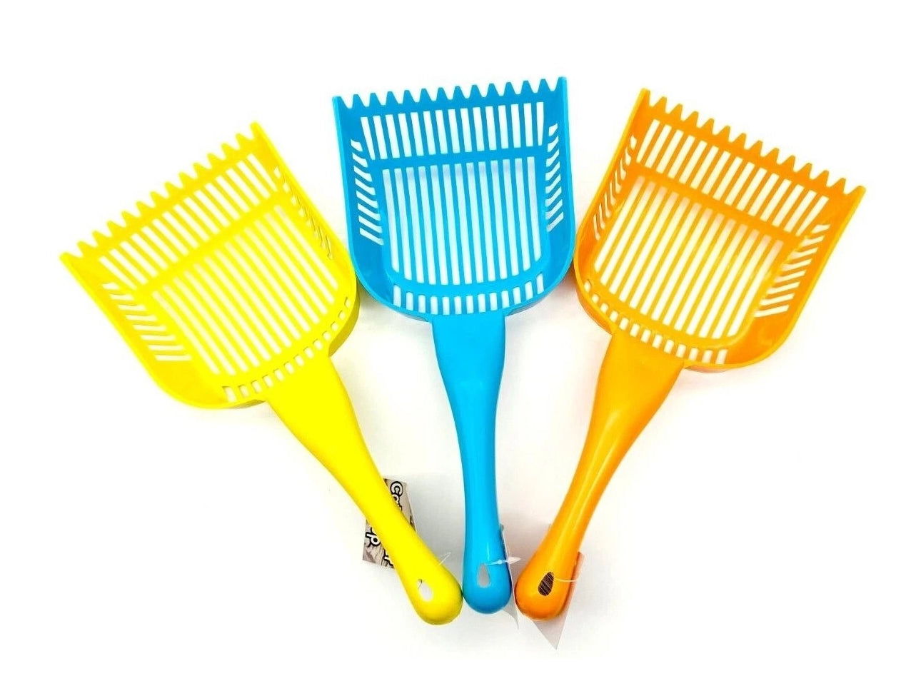 Three plastic litter scoops in yellow, blue, and orange, arranged side by side on a plain white background.